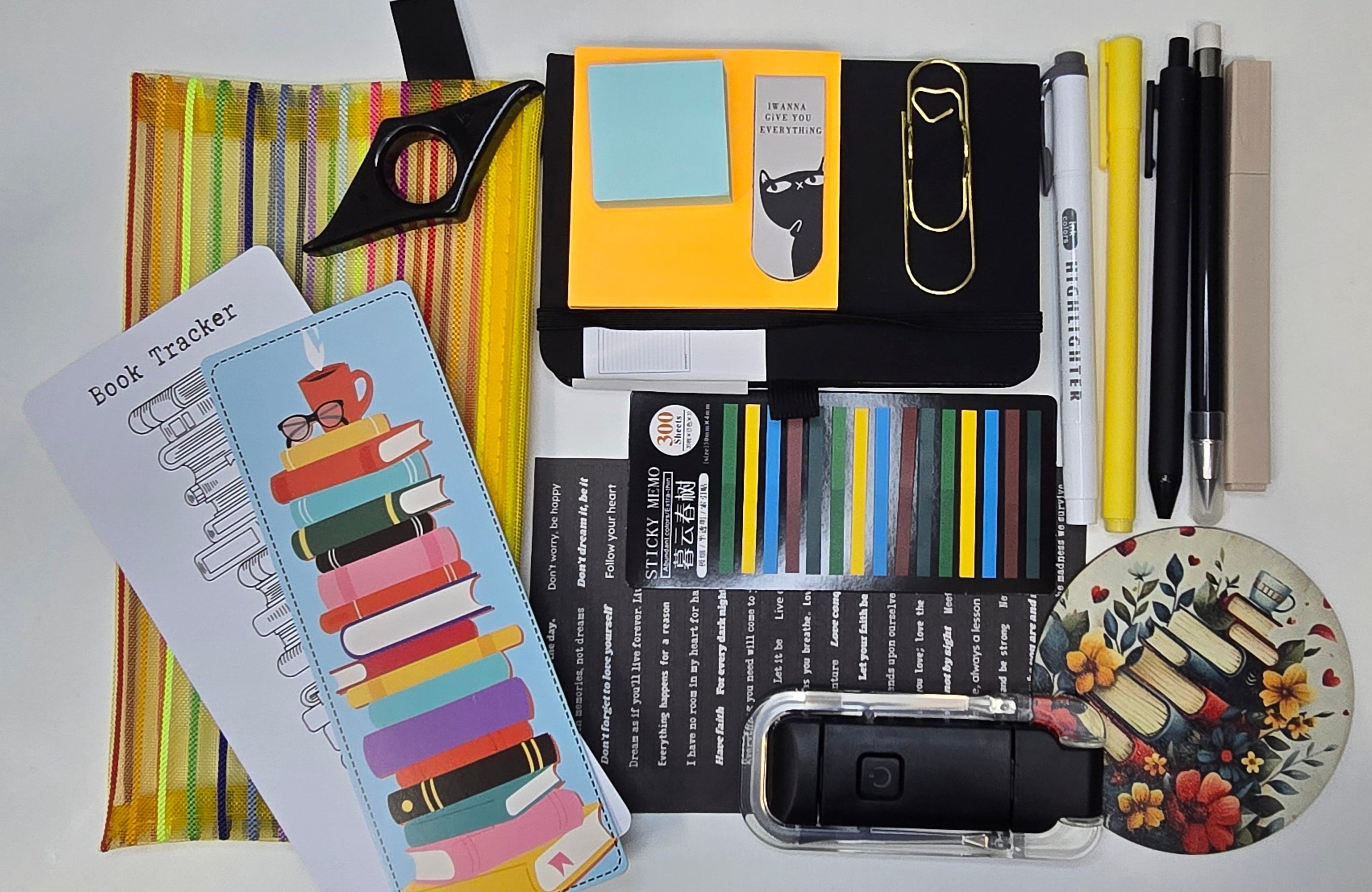 Collection of stationery items including pens, markers, and a notebook on a white surface.